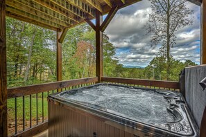 Un bain à remous sous une pergola en bois, avec vue sur les arbres et les collines.