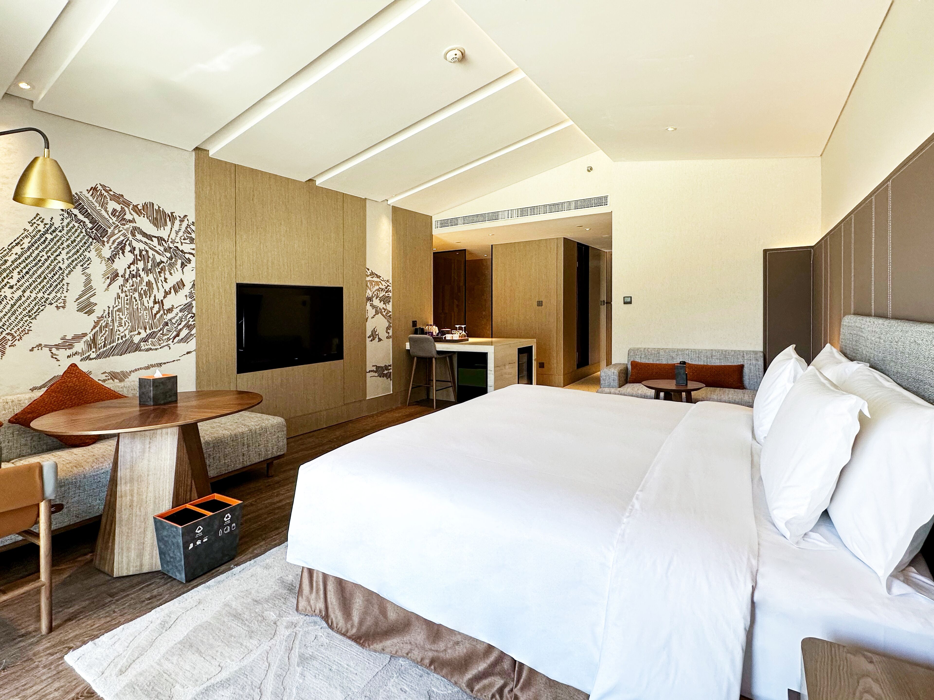 Habitación de hotel moderna con una cama grande, un escritorio, un televisor y una zona de estar con sofá y sillones.