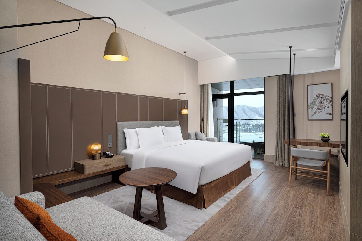 Ein modernes Hotelzimmer mit einem großen Bett, Nachttischen, einem Schreibtisch und Blick auf die Stadt.