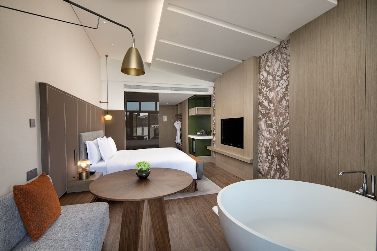 Ein modernes Hotelzimmer mit einem großen Bett, einer Sitzecke mit Couchtisch, einer Badewanne und Blick auf die Stadt.
