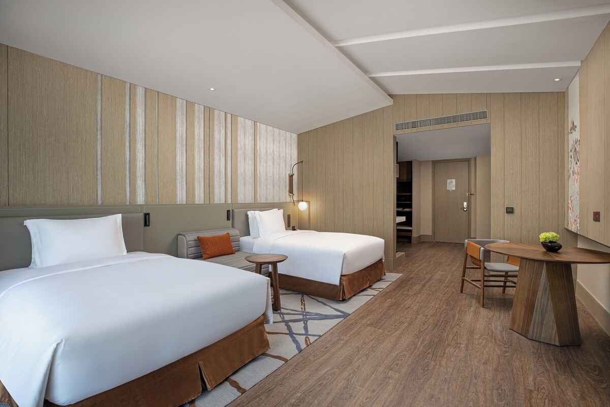A hotel room with two beds, a small table, and a chair.