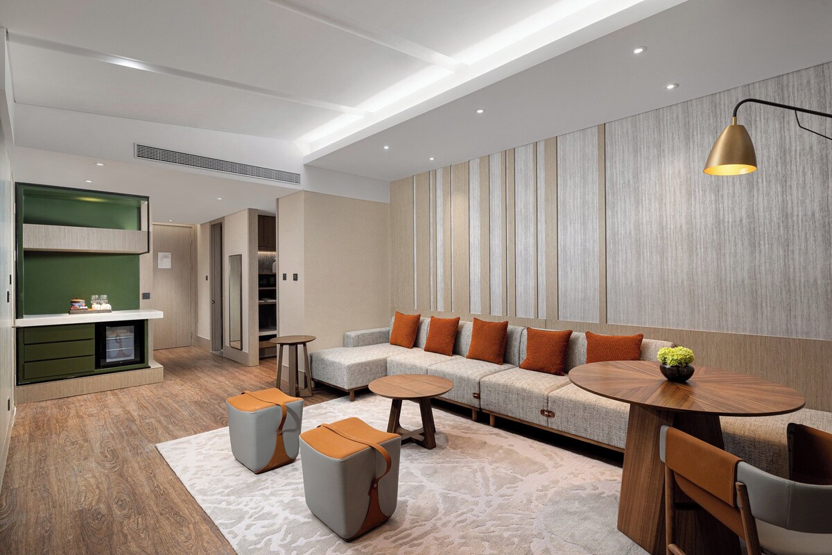 A modern living room with a sectional sofa, a round wooden table, and a green kitchen area.