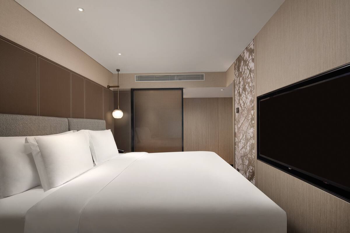 Ein modernes Hotelzimmer mit einem großen Bett, einem flachbildfernseher an der Wand und einem Deckenlüfter.