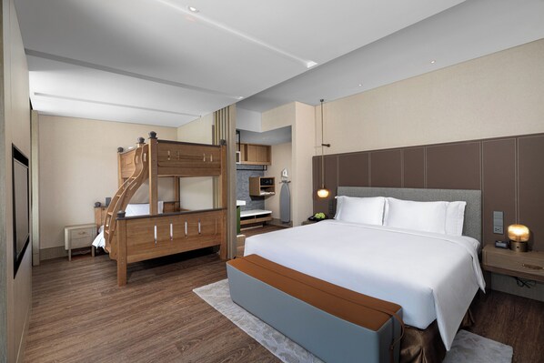 A modern hotel room with a large bed, a wooden staircase, a desk, and a nightstand with a lamp.