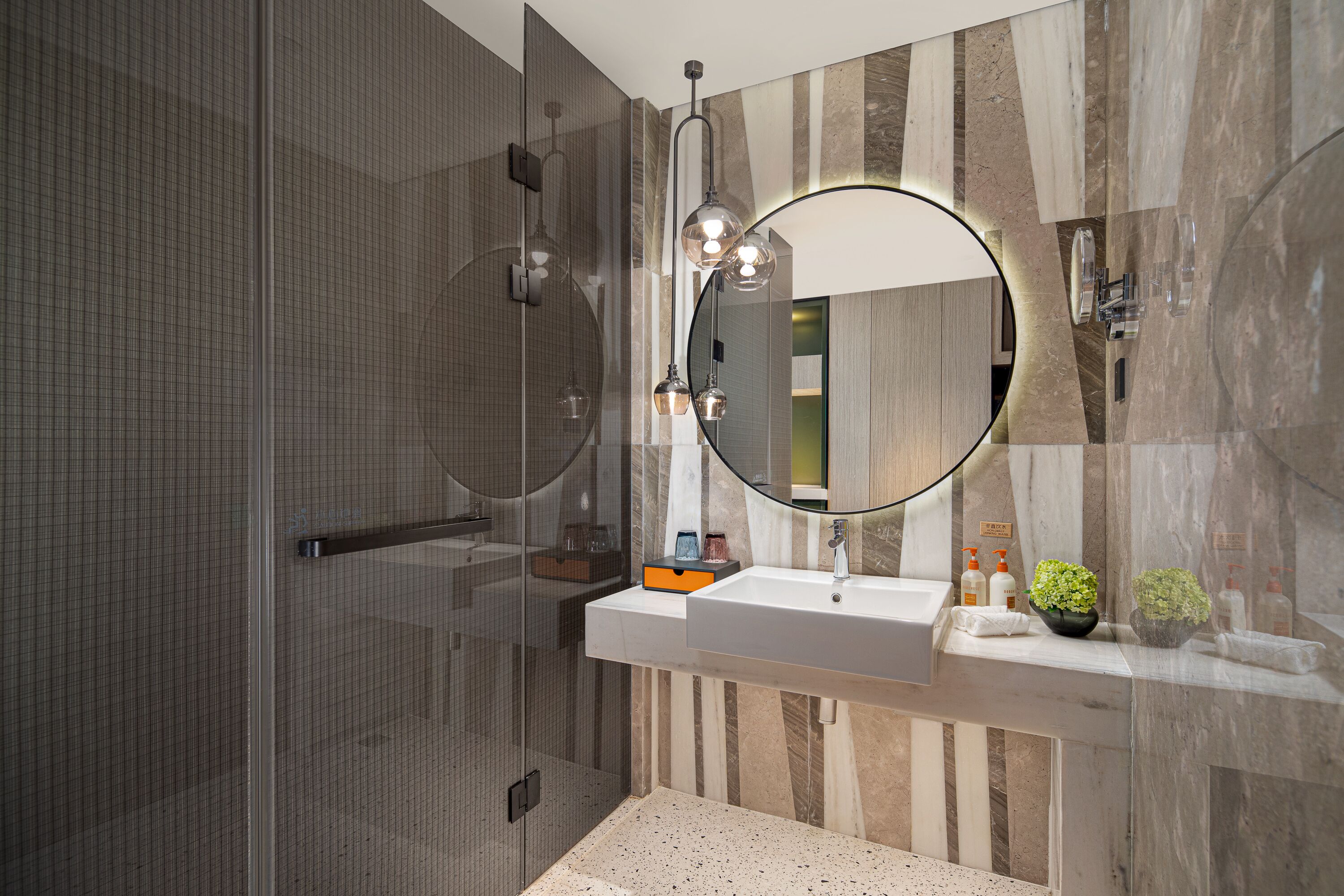 A modern bathroom with a glass shower enclosure, a large mirror, and a vanity with a sink and decorative plants.