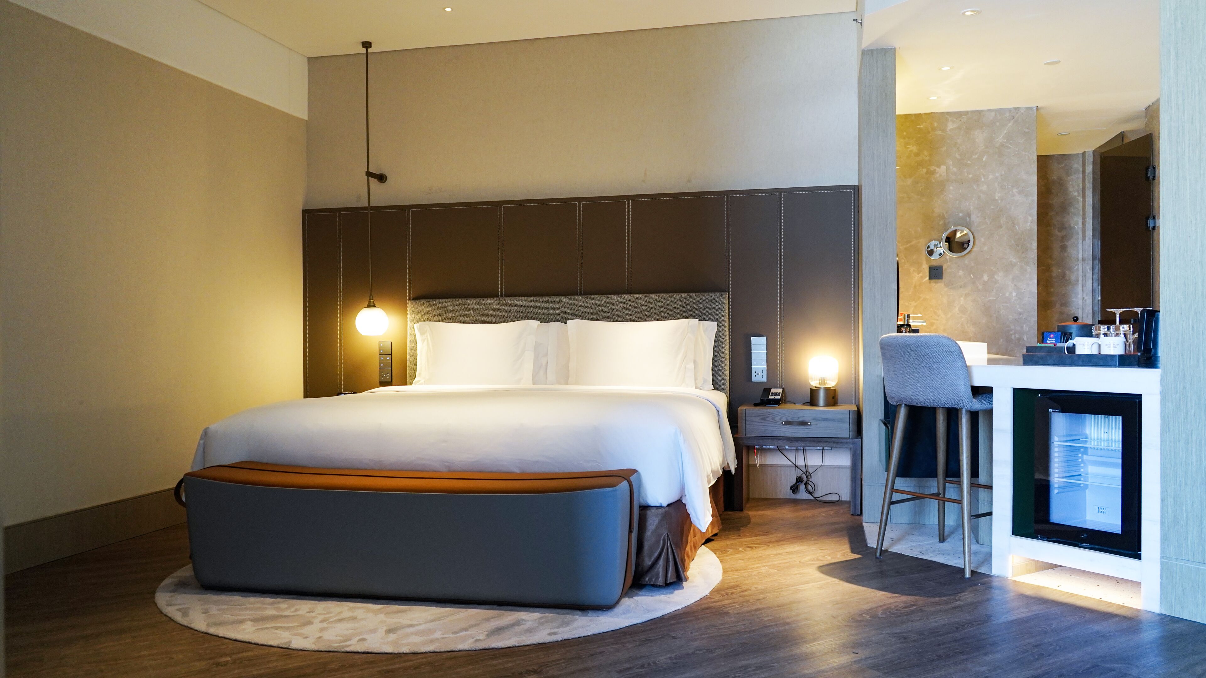 Una habitación de hotel moderna con una cama grande, mesitas de noche, un escritorio con una silla y un minibar.