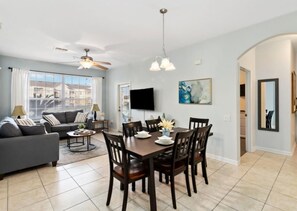A spacious living room with a dark wooden dining table, grey sofa, and a ceiling fan. - Making Memories at Windsor Palms Resort, Great amenities and much more fun! (Kissimmee)