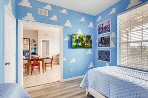 A bedroom with a blue wall, a TV mounted on the wall, and a window with blinds.