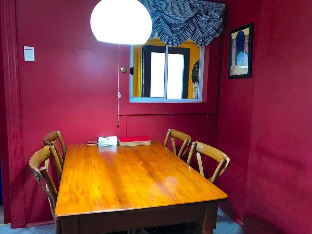 A room with a wooden dining table, four chairs, a window with curtains, and a wall-mounted light fixture.