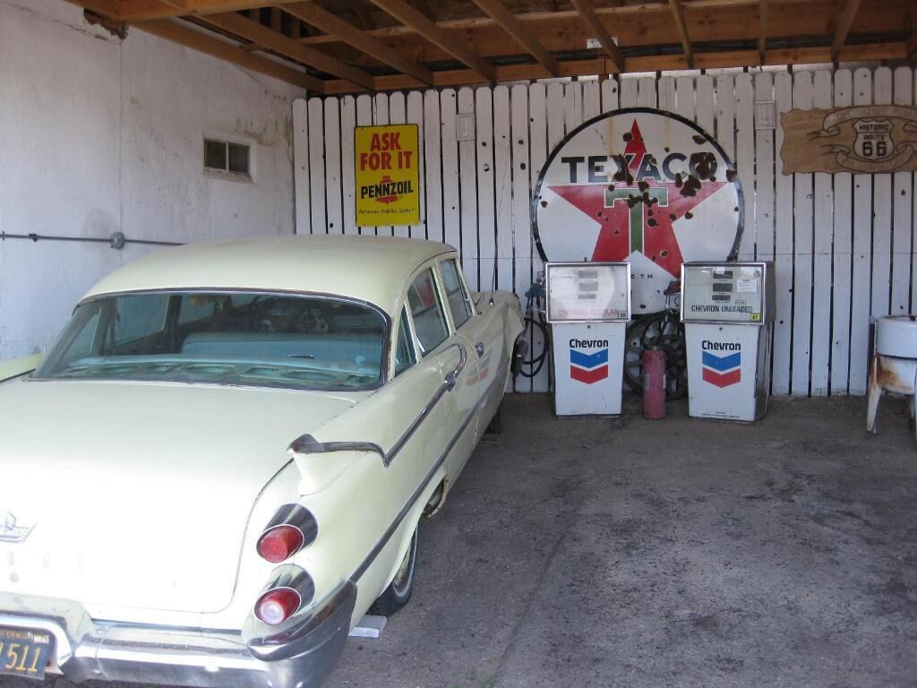 Een oldtimer geparkeerd in een garage met een Texaco benzinepomp en een bord waarop staat: 'Vraag ernaar Pennzoil'.