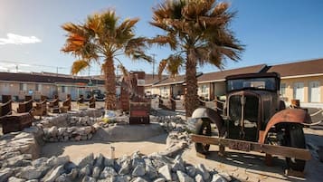 A vintage car parked in front of a building with palm trees and a stone wall.