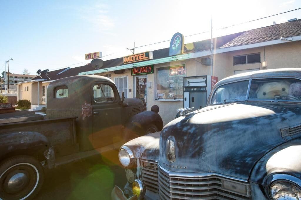 Un motel d’époque, avec une pancarte « CHAMBRES LIBRES », une voiture classique garée devant et une pancarte « OUVERT » au-dessus de l’entrée.