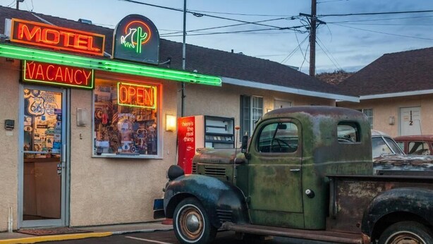 A vintage motel with neon signs, a vintage truck parked in front, and a vintage Route 66 sign on the pavement. - Route 66 Motel (Barstow)