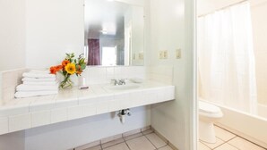 A bathroom with a white sink, mirror, and toilet. There is a vase with flowers on the sink counter. - Route 66 Motel (Barstow)