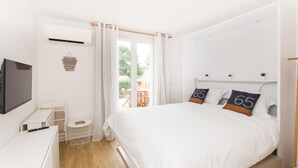 Ein Schlafzimmer mit einem Bett, einem Schreibtisch, einem Sessel, einem kleinen Tisch und einer Klimaanlage.
