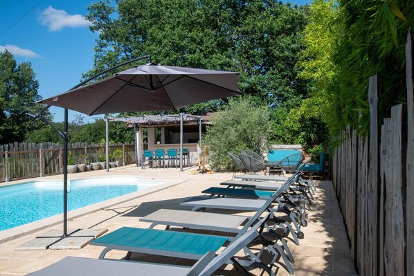 A swimming pool area with lounge chairs, a covered seating area, and a wooden fence. - Gîte Bouconne, air-conditioned studio with a terrace for 1 or 2 people - shared outdoor pool (Pujaudran)