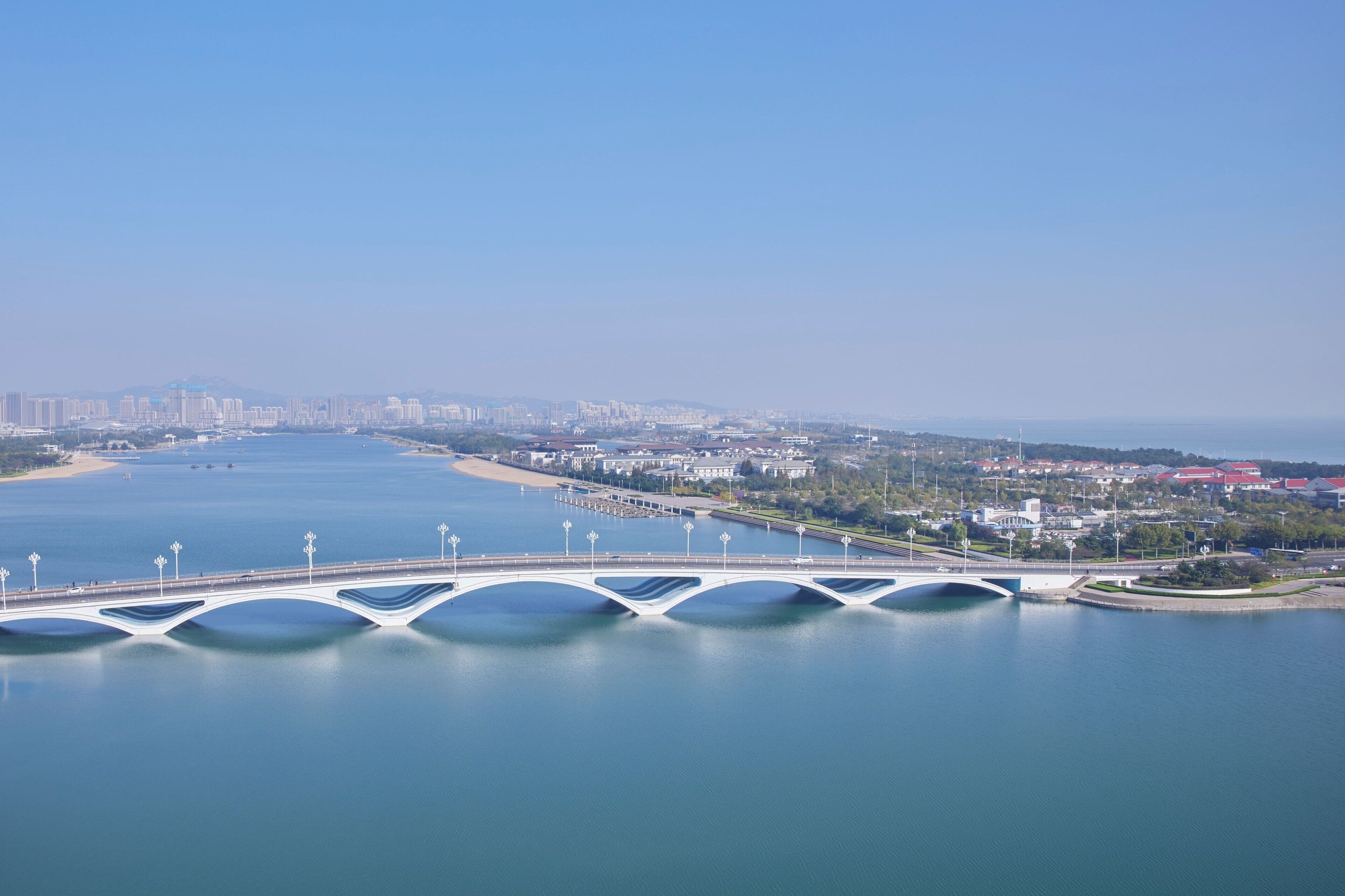 A white bridge with multiple arches over a calm body of water, connecting two land masses.
