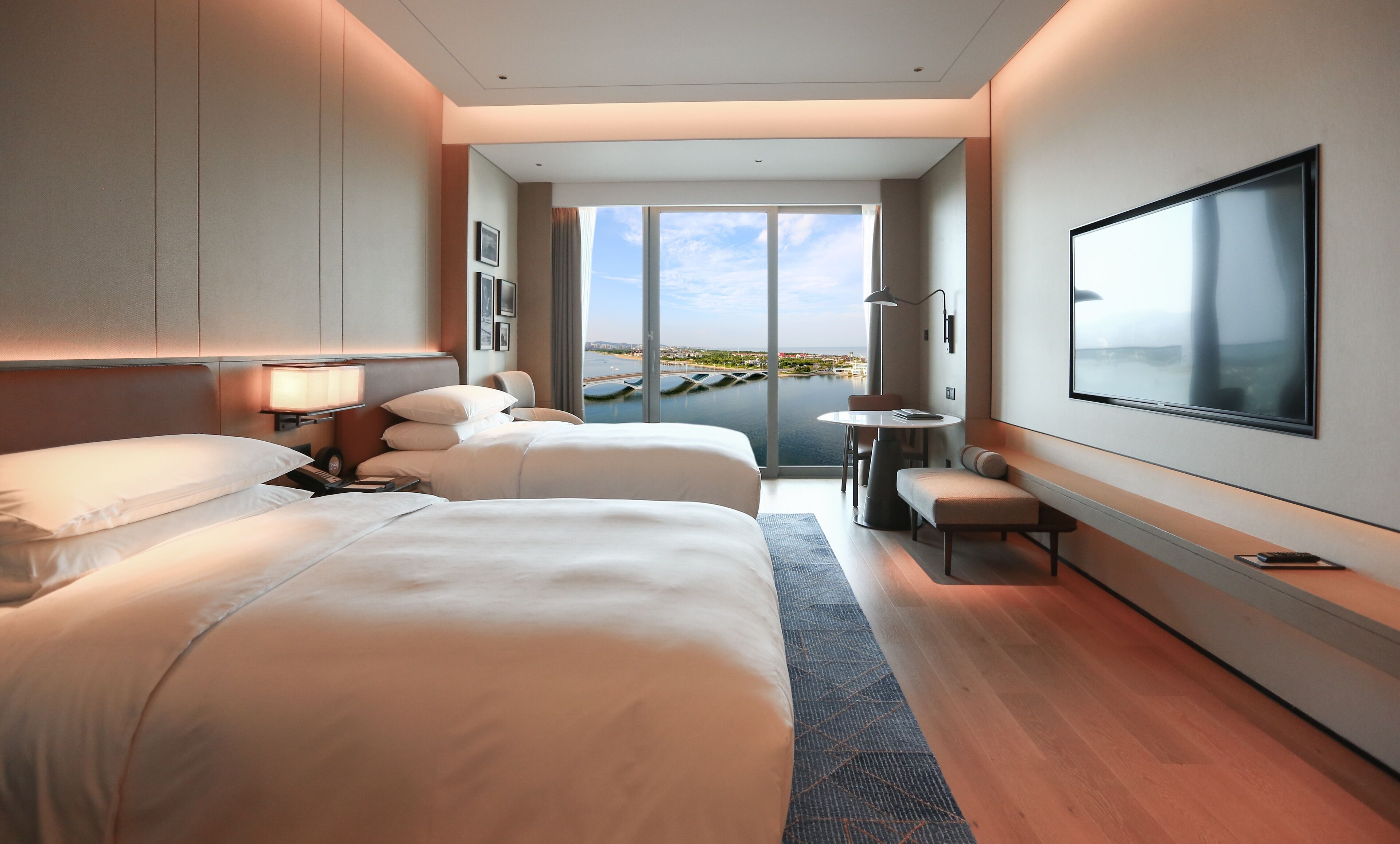 A modern hotel room with two beds, a desk, and a large TV.