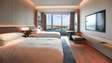 A modern hotel room with two beds, a desk, and a large TV.