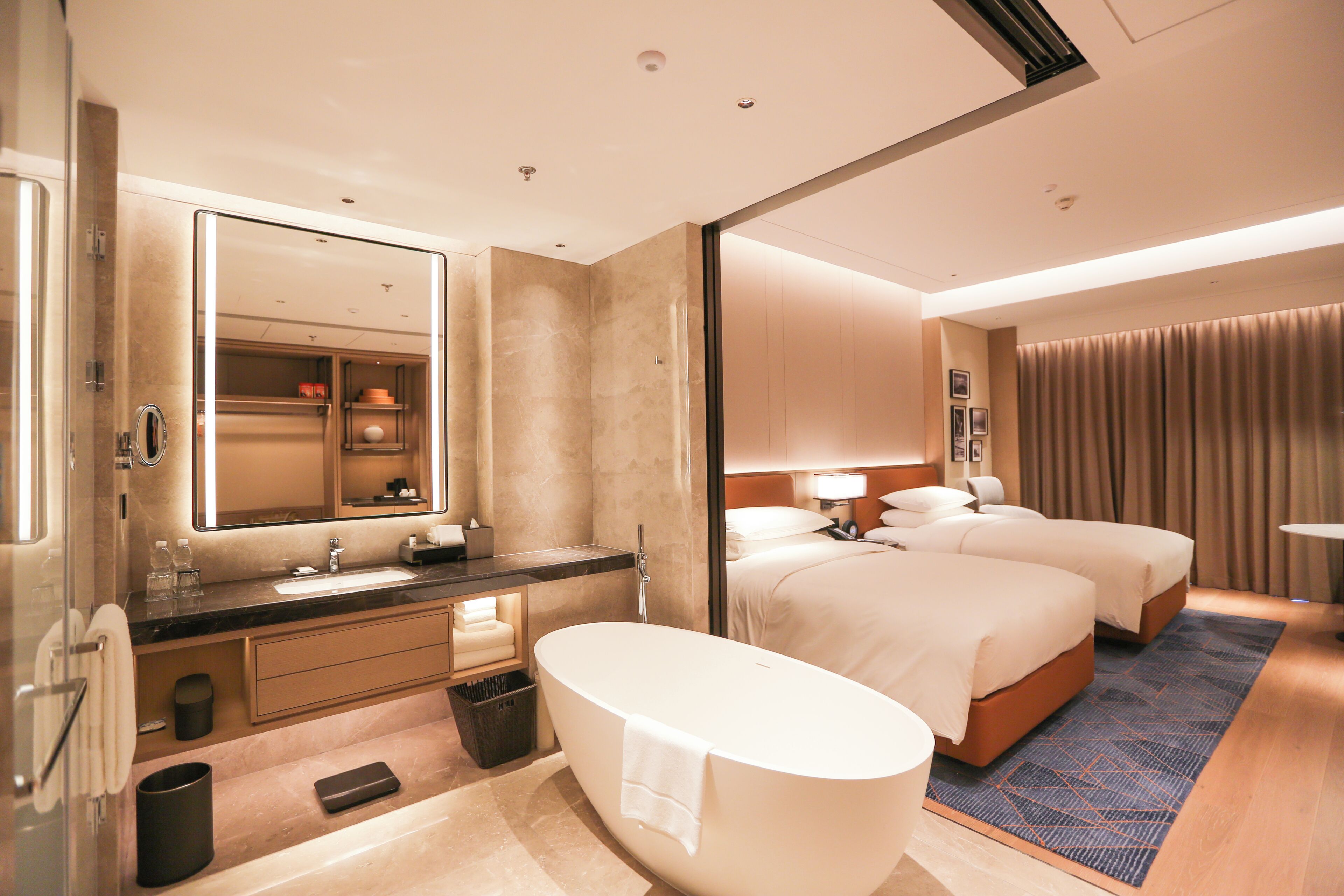 Une chambre d’hôtel dotée d’une grande baignoire, d’un lit double, d’un lit simple, d’une coiffeuse avec un miroir et d’une salle de bain avec des toilettes et un lavabo.