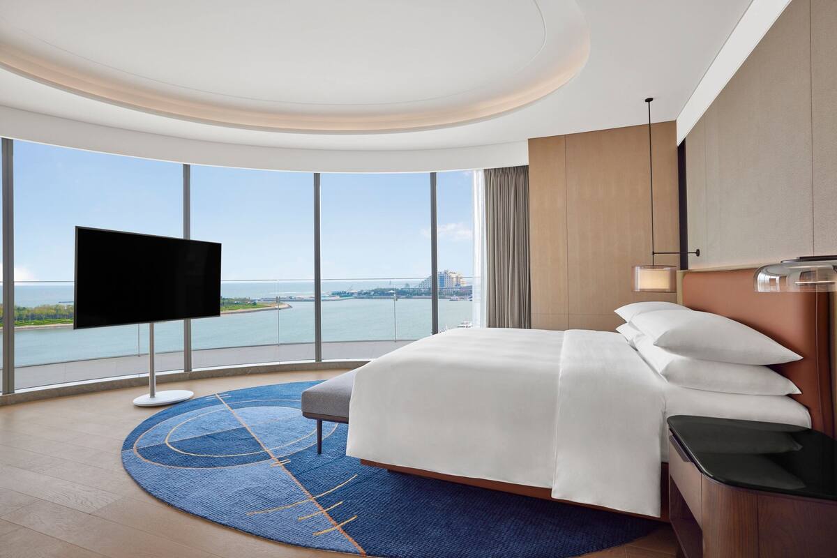 A hotel room with a large bed, a TV, a view of the water, and a modern design.