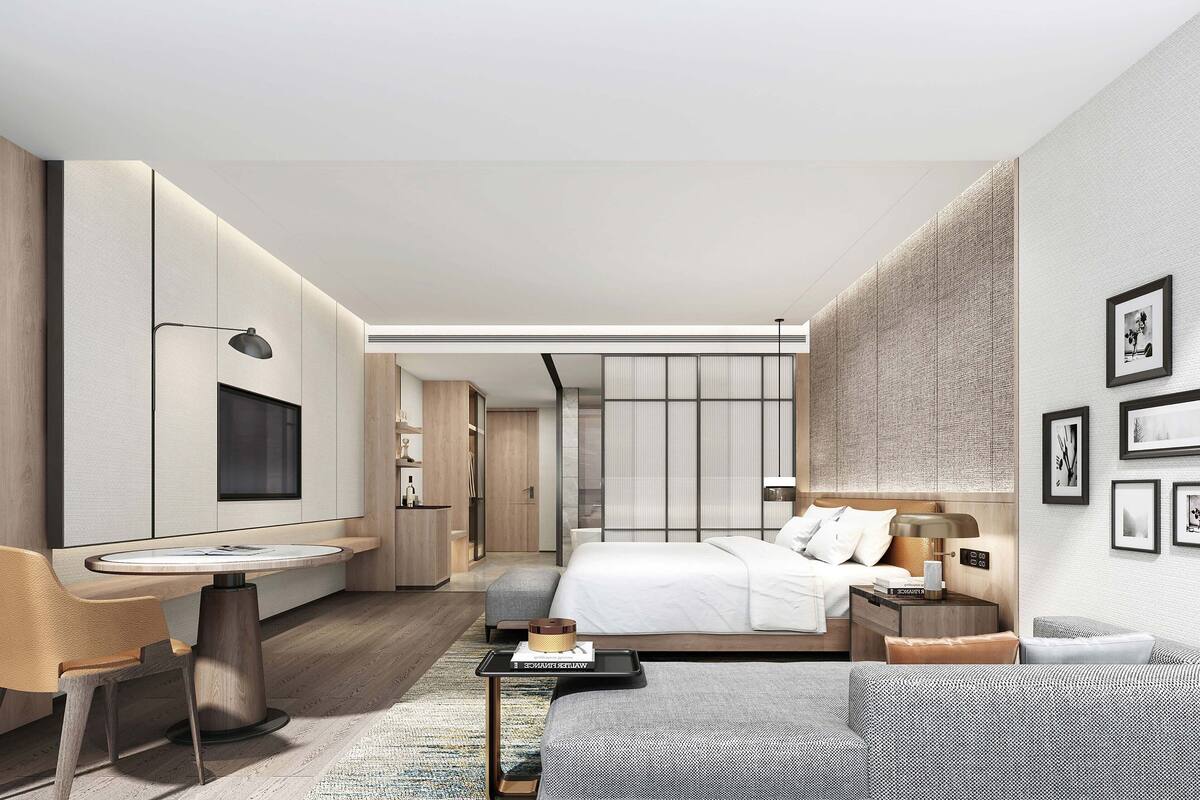 A modern hotel room with a bed, a desk, a chair, a sofa, and a TV.