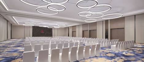 A conference room with rows of white chairs, a patterned carpet, and modern circular ceiling lights.