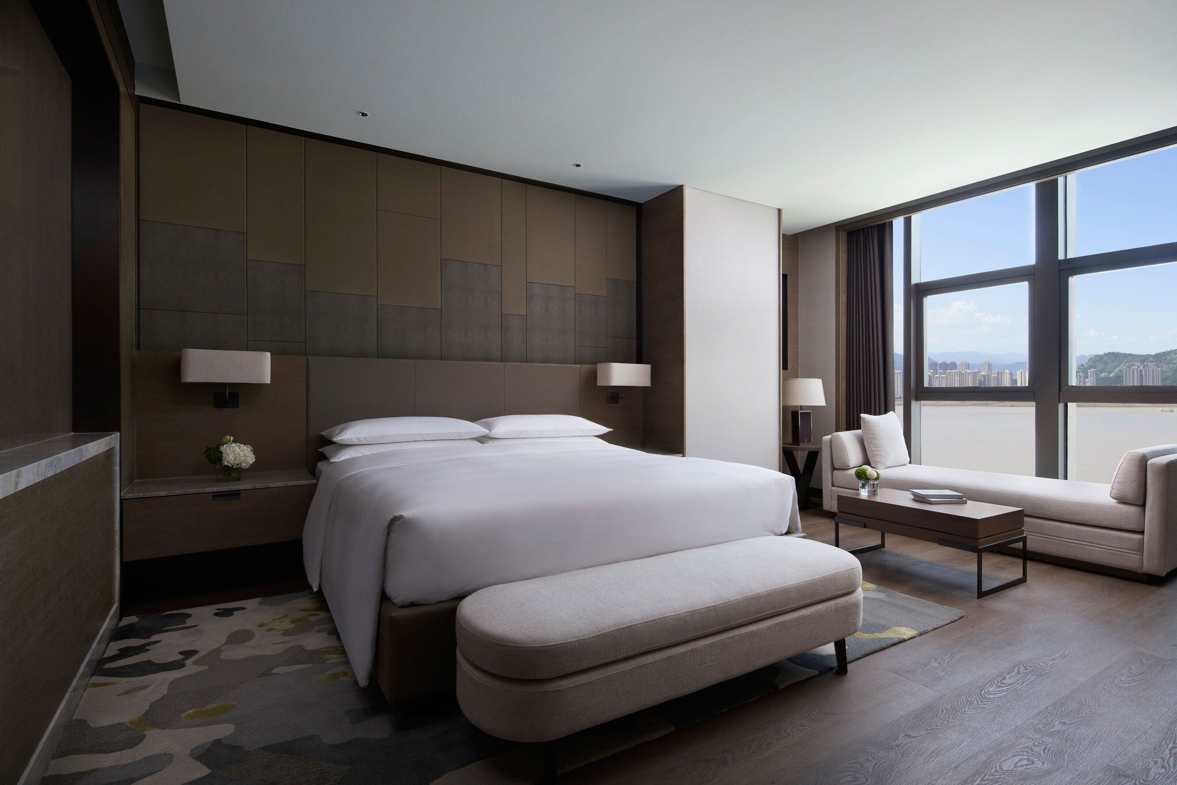 A modern hotel room with a large bed, a sofa, and a view of the city.