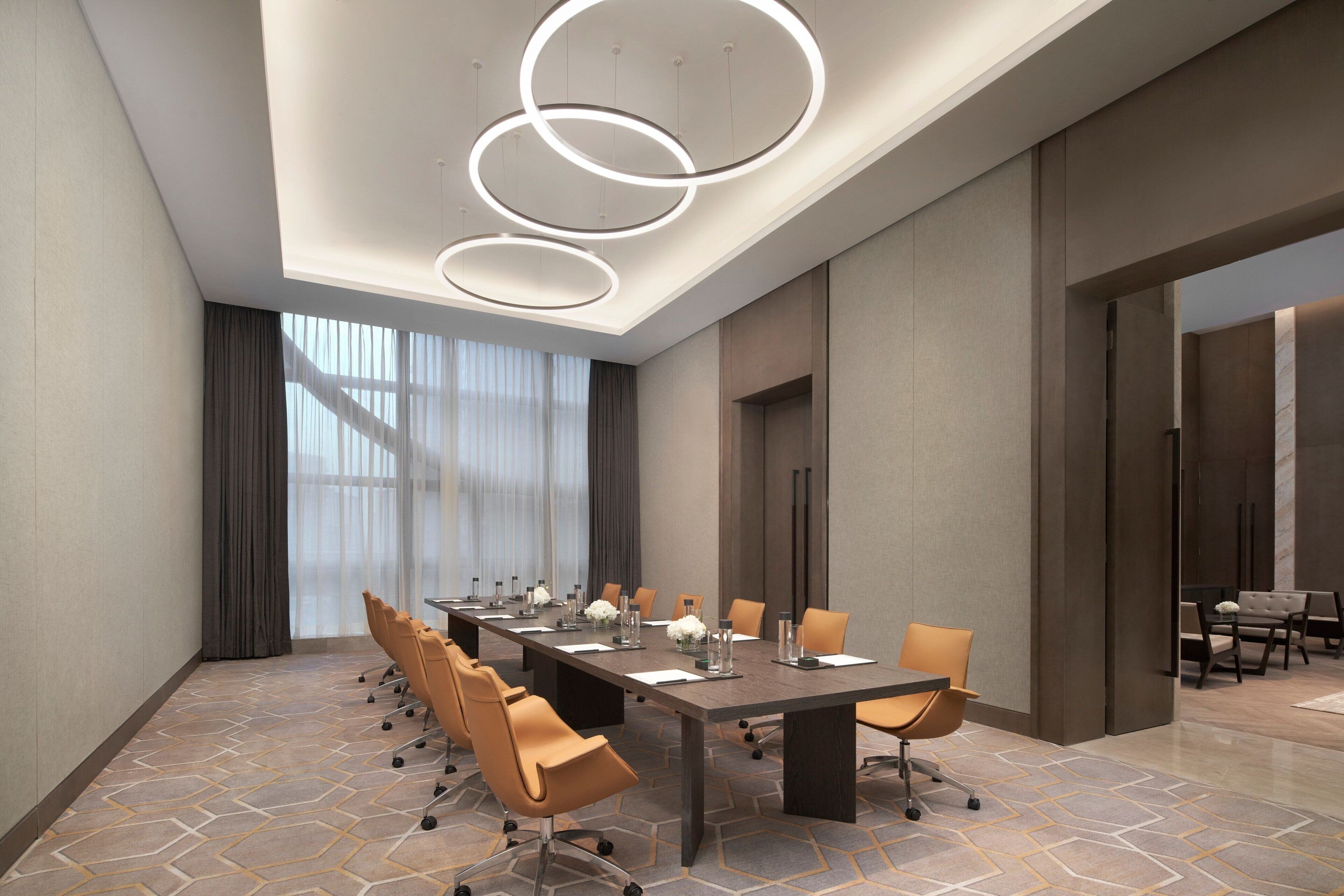 A modern conference room with a long table, multiple chairs, and a ceiling with circular light fixtures.