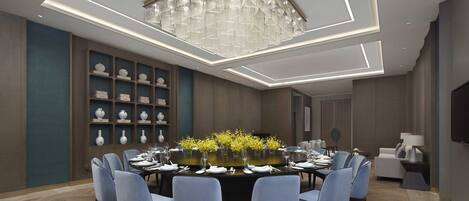 A modern dining room with a round table, blue chairs, and a decorative chandelier.