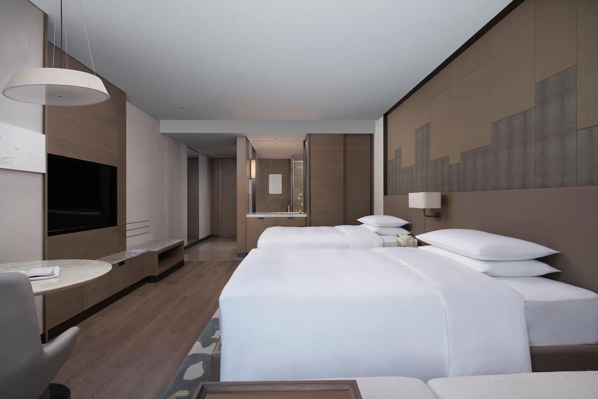 A hotel room with a large bed, a desk, a TV, and a bathroom visible through an open door.