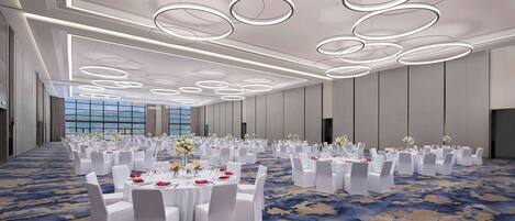 Un amplio salón de banquetes bien iluminado con mesas redondas dispuestas para un evento formal, con alfombra estampada y un diseño moderno del techo.