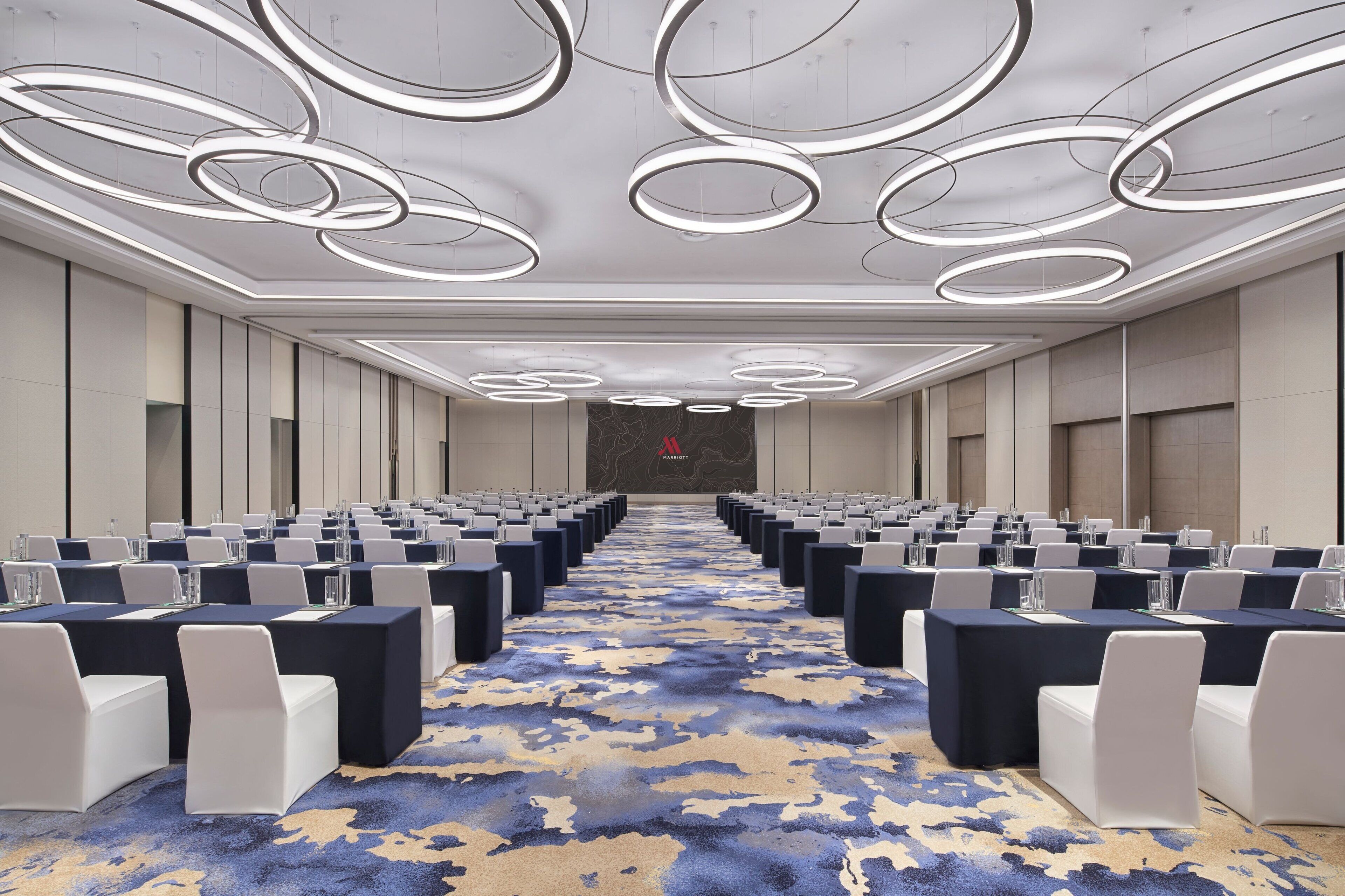 A conference room with rows of tables and chairs, a patterned carpet, and a modern ceiling design.