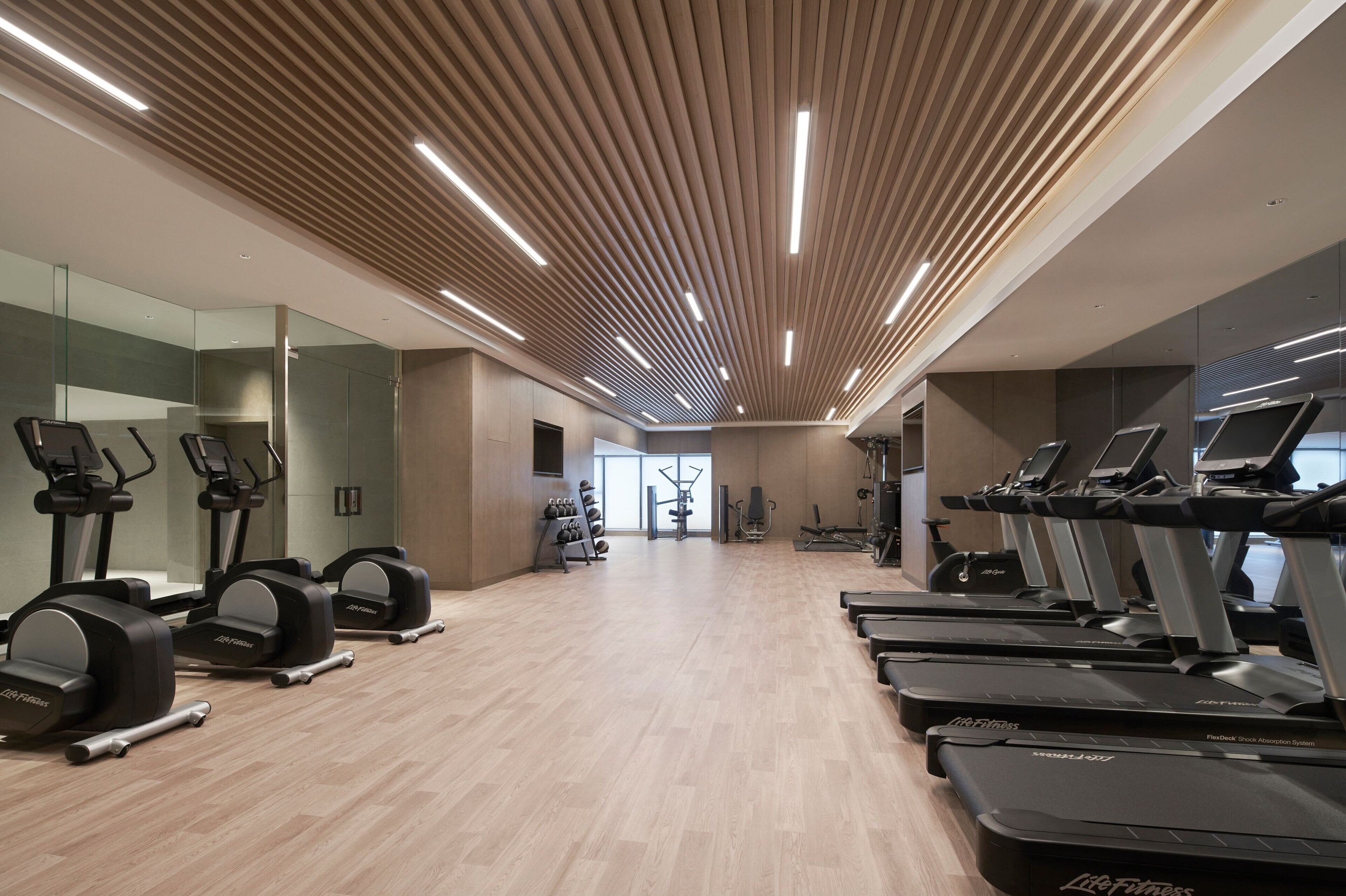 A modern gym with treadmills, elliptical machines, and weight equipment.