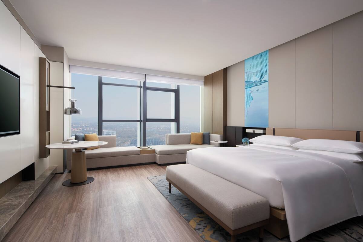 A modern hotel room with a large bed, a sofa, a small table, and a TV.
