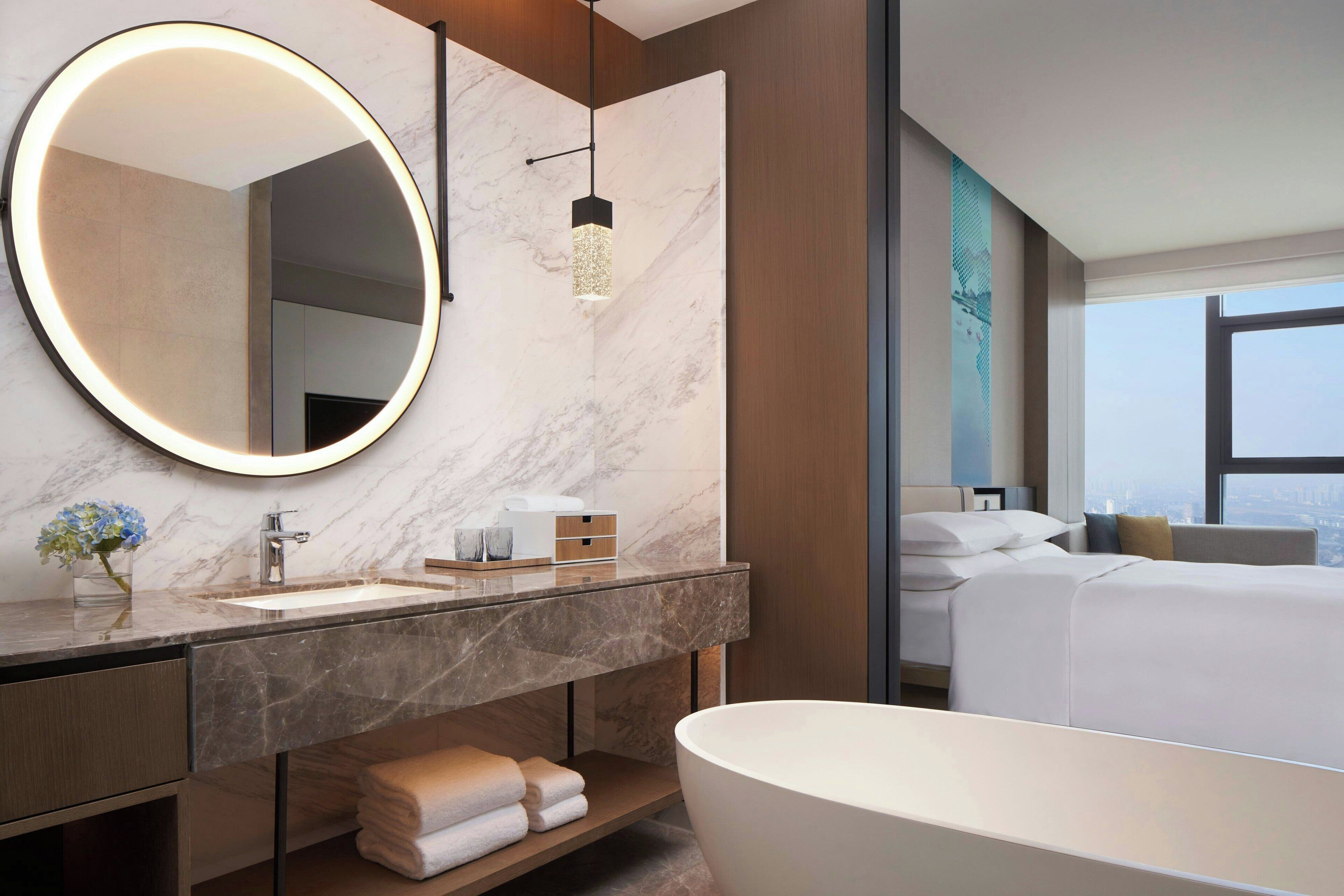 Un baño moderno con un espejo redondo grande, una bañera independiente y una encimera de mármol.