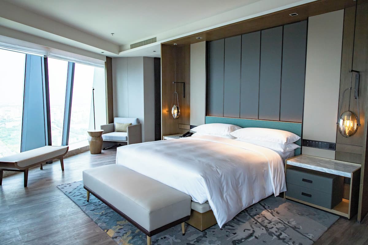 A modern hotel room with a large bed, bedside tables, a bench, and a view of the city.