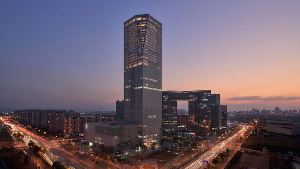 A high-rise building with a modern architectural design, surrounded by other buildings and busy streets at dusk. - Jinhua Marriott Hotel (Jinhua)