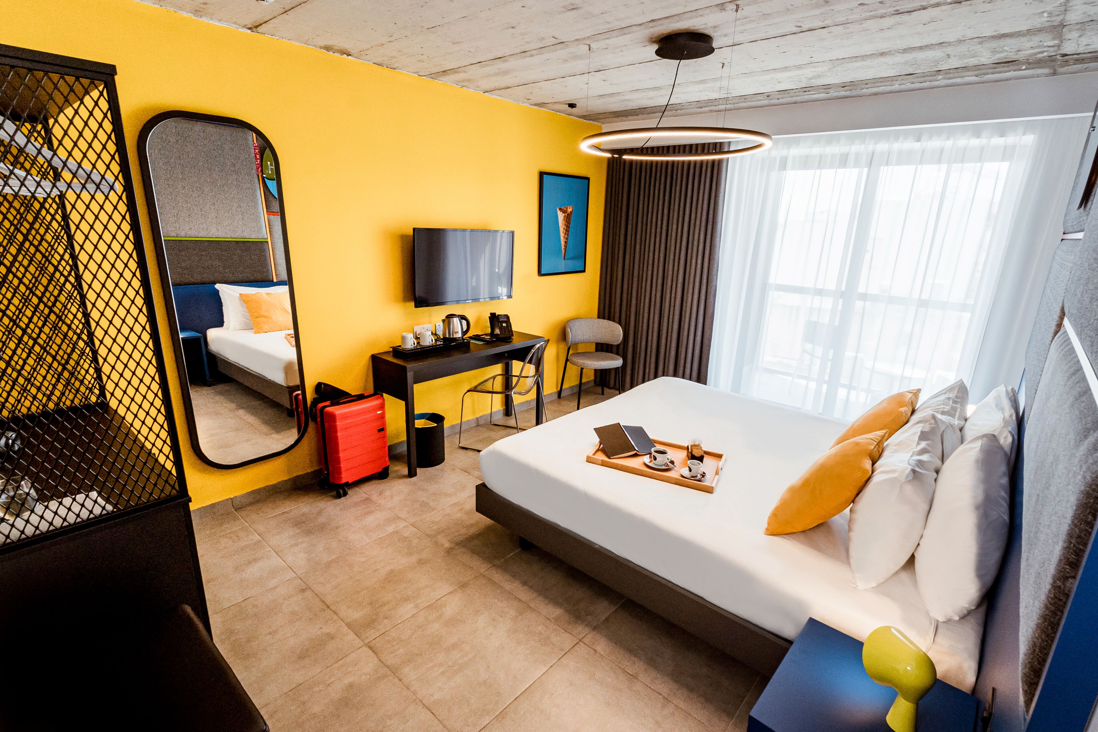 A hotel room with a bed, a desk, a chair, a TV, and a window with curtains.