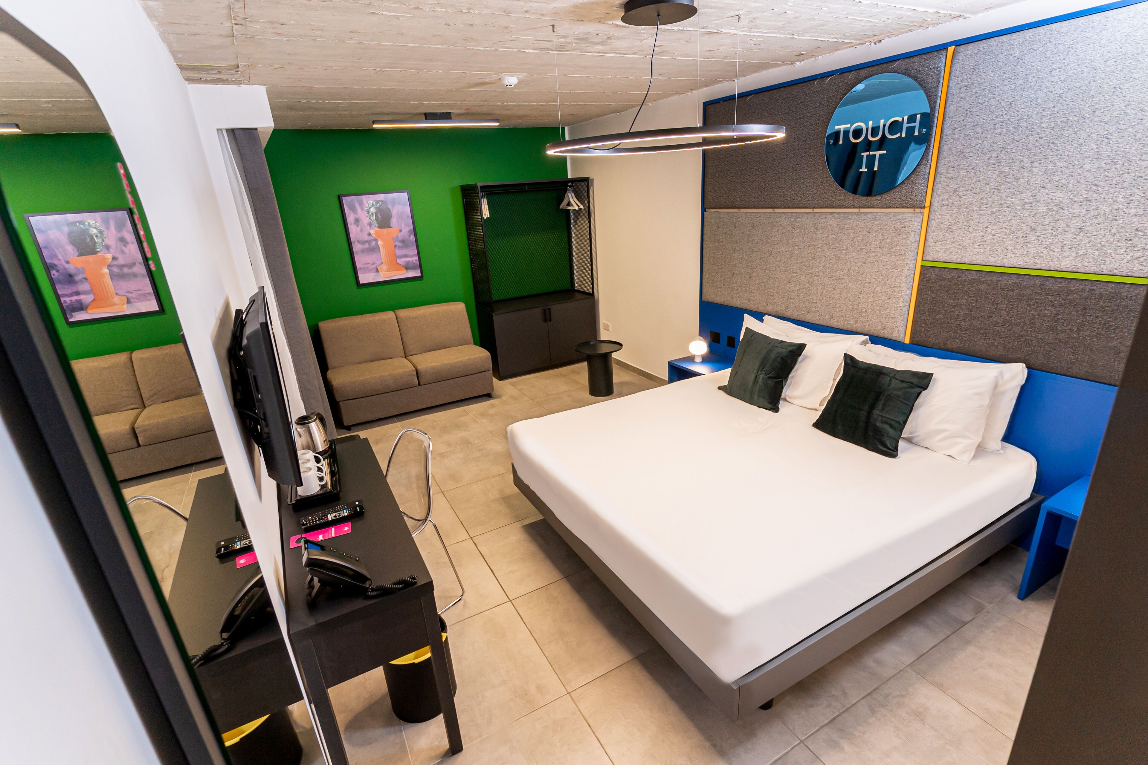 Una habitación de hotel moderna con una cama grande, un sofá, un escritorio con cafetera y televisión.