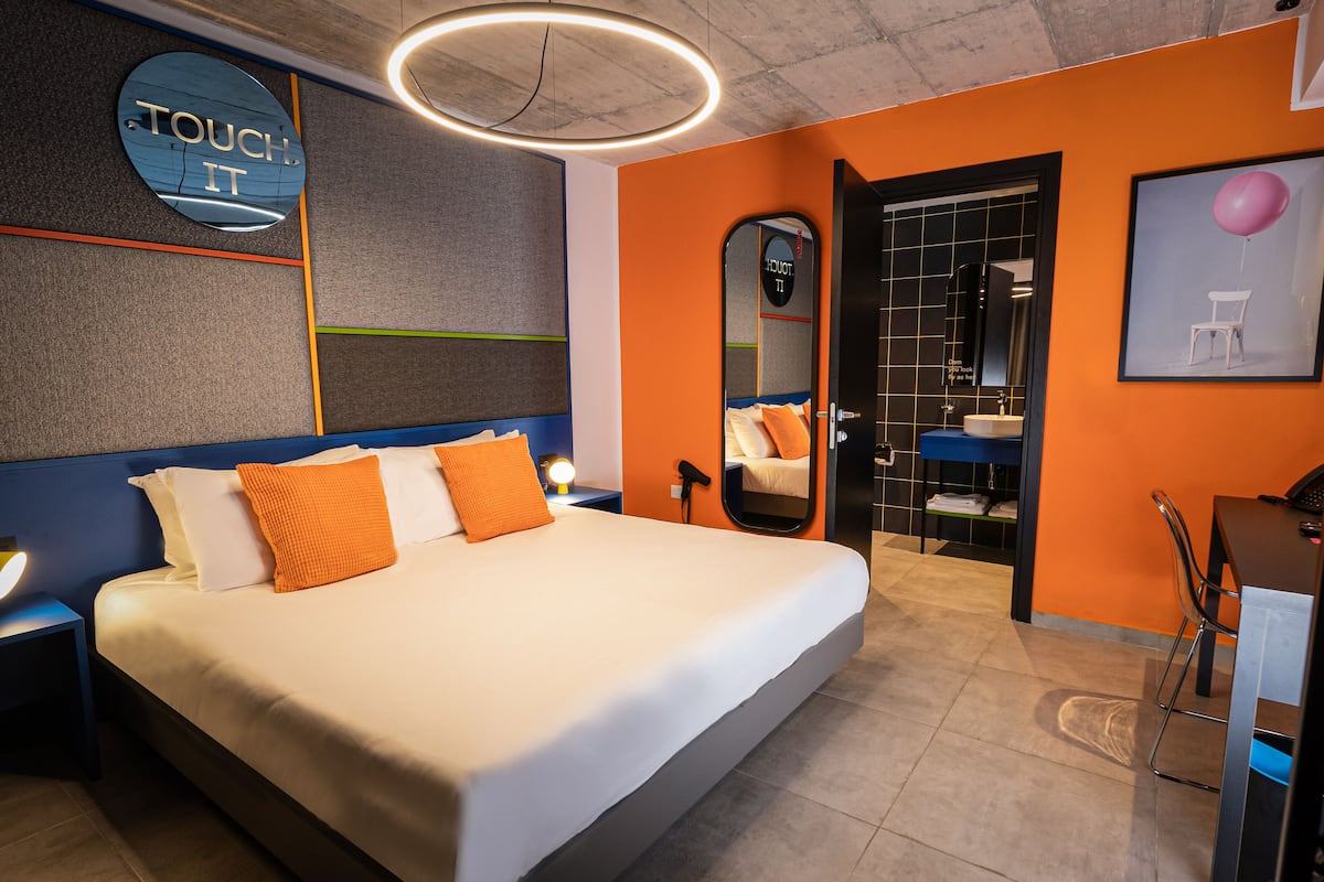 A modern hotel room with a large bed, a desk, and a bathroom with a mirror and sink.