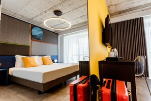 Habitación de hotel con una cama grande, un escritorio, una silla, una maleta y un televisor.