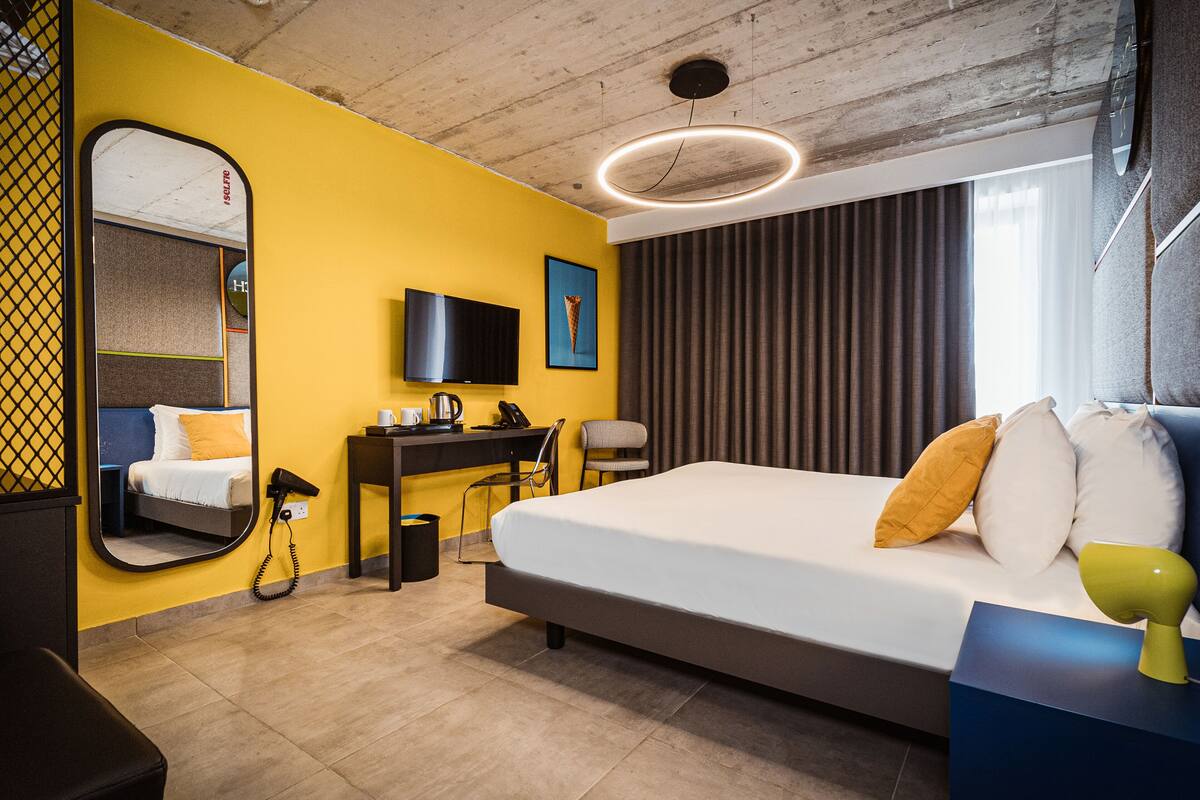 A hotel room with a bed, a desk, a chair, a television, and a large mirror.