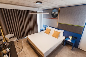 A modern hotel room with a large bed, a desk with a coffee maker, a chair, and a wall-mounted TV. - IKYK Hotel - IK Collection (St. Julian's)