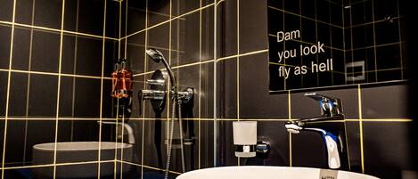 Un baño con pared de azulejos negros, un lavabo blanco y un espejo con un letrero.