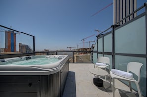 A rooftop terrace with a hot tub, two white chairs, and a glass wall offering a view of the cityscape and construction cranes. - IKYK Hotel - IK Collection (St. Julian's)