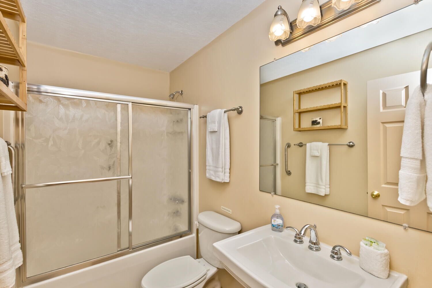 A bathroom with a shower, toilet, sink, and a large mirror.