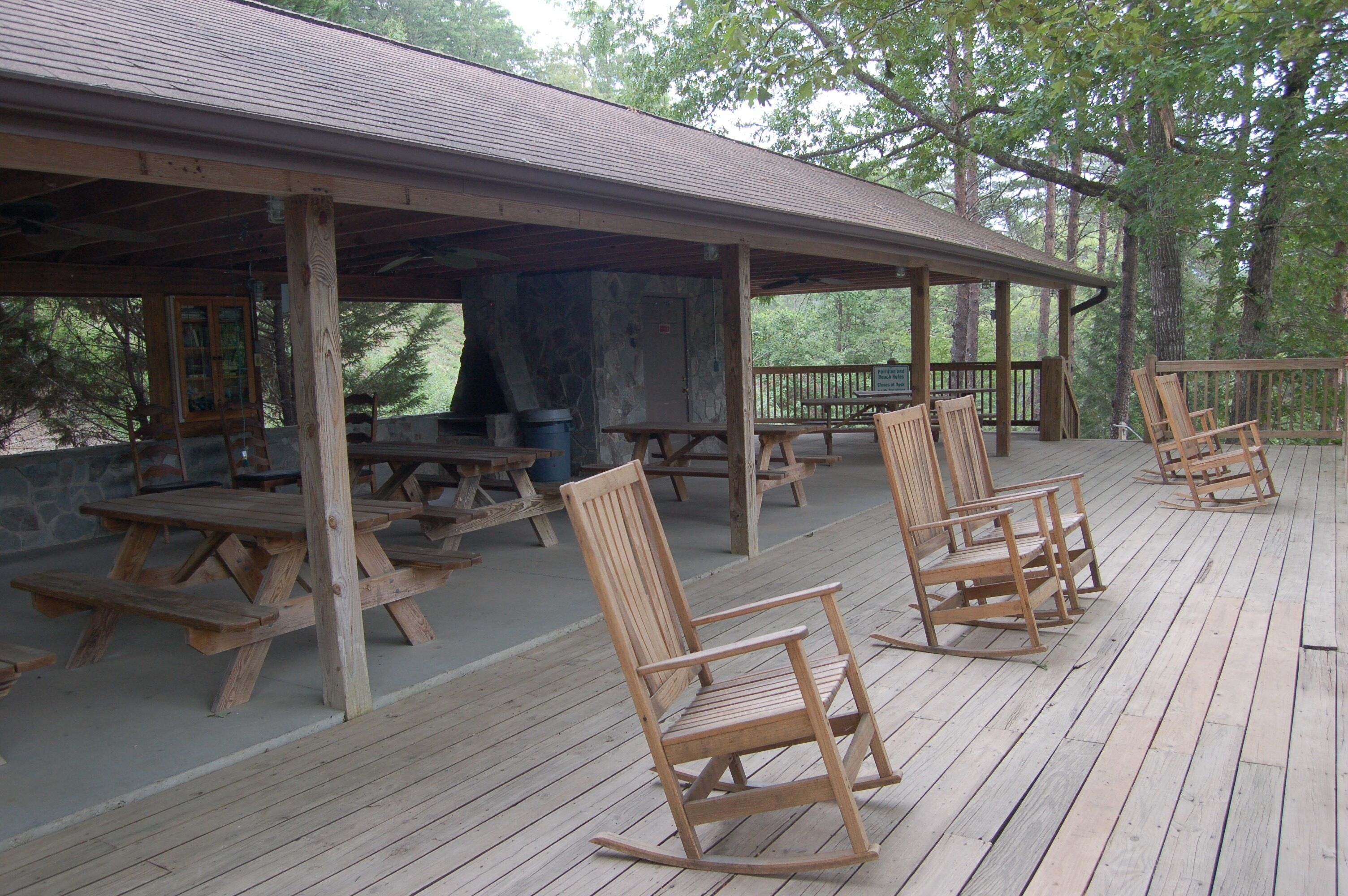Un espace pique-nique abrité, doté de bancs et de tables en bois, et entouré d’arbres.