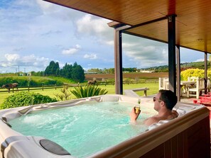 A man relaxing in a hot tub with a view of a rural landscape.