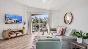Ein modernes Wohnzimmer mit großem Fernseher, einer Couch, einem Couchtisch und Blick ins Freie.